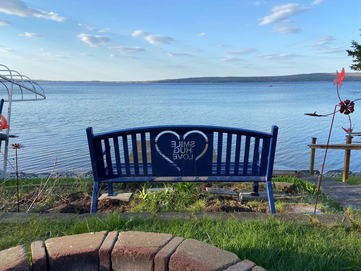 A navy blue bench with an open heart reading Smile Hug Love, placed on the shores of a lake in Michigan — the last place Amy visited before the accident