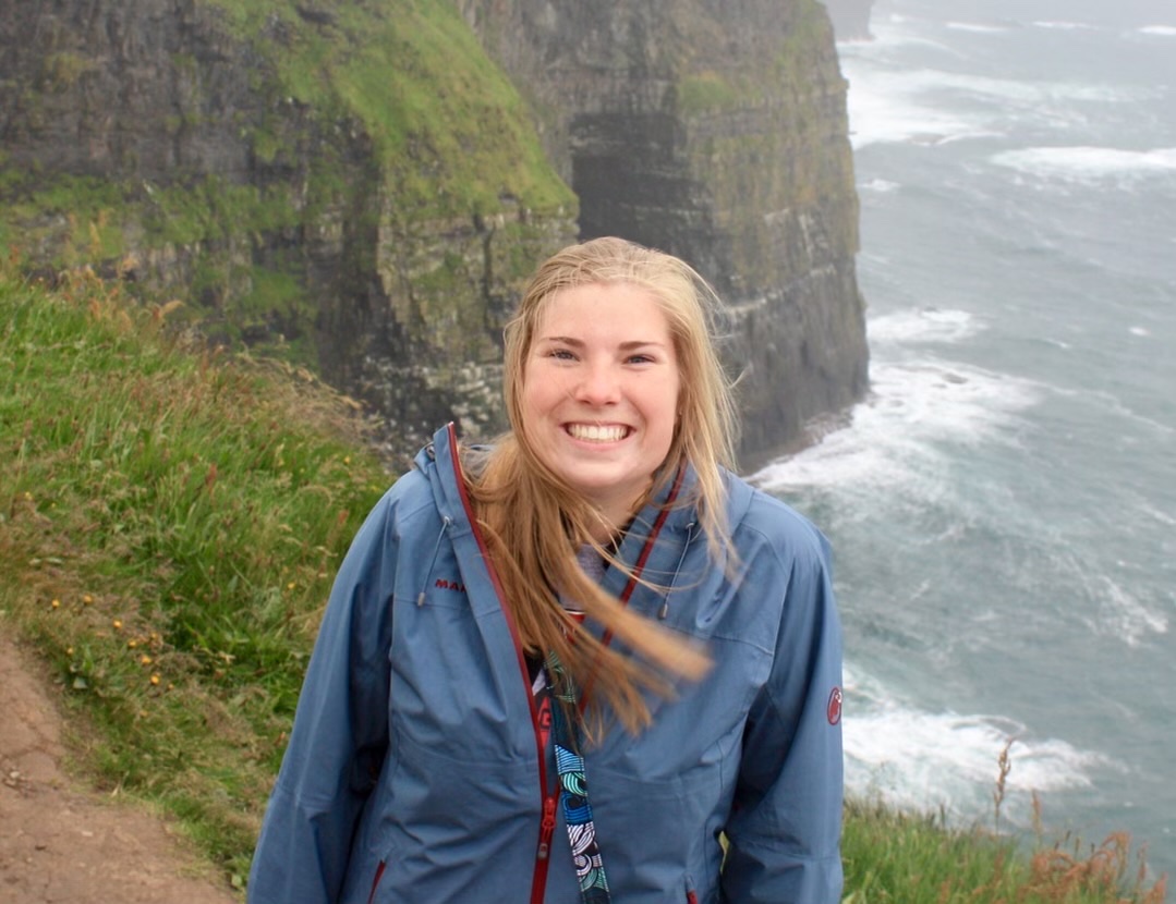 Amy Lee smiling at the Cliffs of Moher, Ireland — her hair blowing in the wind, the Atlantic Ocean behind her